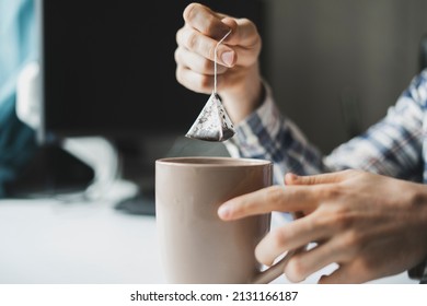 Person's Hand Holding A Tea Bag And Making Hot Cup Of Tea