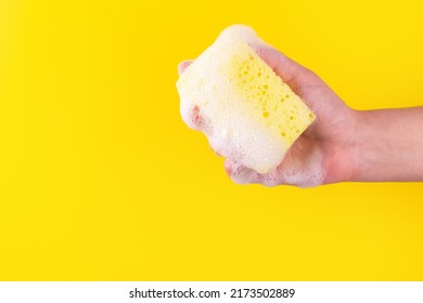 Persons hand holding yellow sponge for dish wash. Washcloth covered in soap. Domestic chores and supplies concept. Sensitive dishwashing detergent. Copy space in left side. Isolated on yellow - Powered by Shutterstock