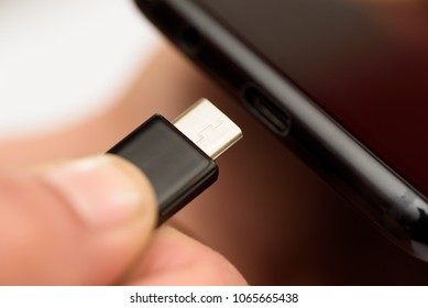 Persons hand inserting a USB cable charger into a mobile phone