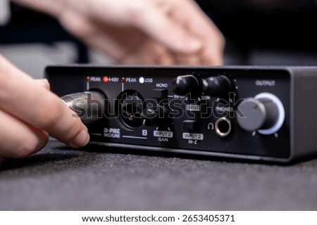 A person's hand inserting an XLR microphone cable into a studio audio interface, crucial for high-quality music production, live streaming, and podcast recording at home