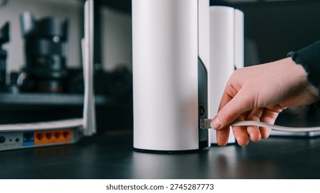 A person's hand inserts an Ethernet cable into a sleek, white mesh Wi-Fi node, suggesting network setup or expansion - Powered by Shutterstock - Get 15% off with code: PIKWIZARD15