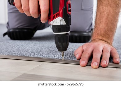 Person's Hand Installing Carpet On Floor Using Wireless Screwdriver