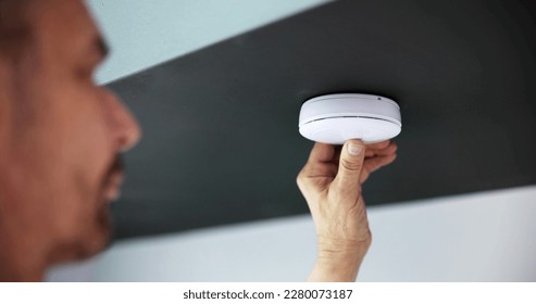 Person's Hand Installing Smoke Detector On Ceiling Wall At Home