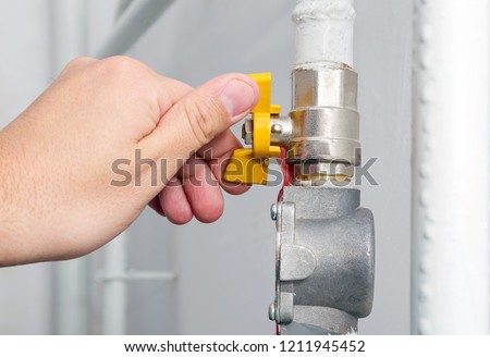 Person's hand opens or closes yellow gas valve on gas pipe at home. Symbolic image of natural gas savings in the heating season. Part of body, selective focus.