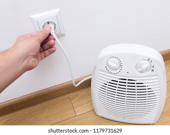 Person's Hand Plug In Electric Heater In The Socket. 