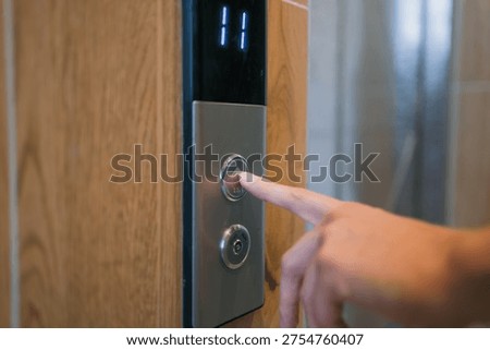 Person's hand pressing an illuminated elevator call button, selecting to go up to the eleventh floor, representing travel, business, and daily commuting in a contemporary setting