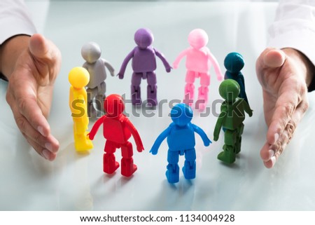 A person's hand protecting multi colored human figures forming circle