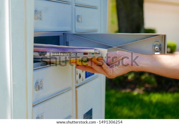 Person\'s hand pulling a pile of junk mail out of\
an outdoor community\
mailbox
