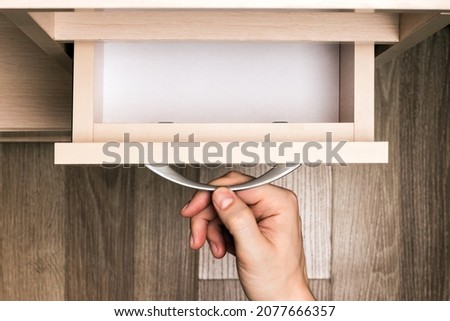 Person's hand pulls out a pull-out empty furniture drawer
