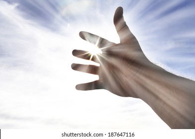 Persons hand reaching in hope towards heaven with sunlight shining through