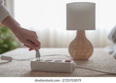 Person's hand removing an electrical plug from a white multiple socket power strip, showing responsible energy management and reducing electricity consumption at home