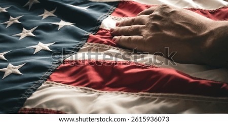 a person's hand resting on a United States flag. reverence and honor patriotic banner. natural waves and ripples in the fabric with embroidered stars. banner or design element.