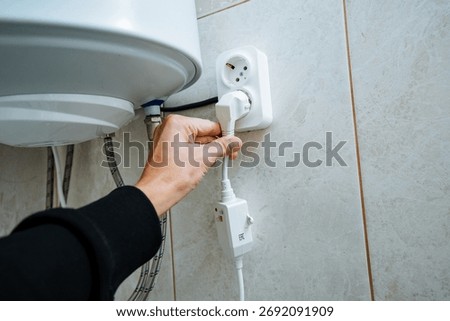 A persons hand is shown plugging in an electrical appliance to a wall socket next to a water heater, showcasing the importance of proper electrical connections in home installations.