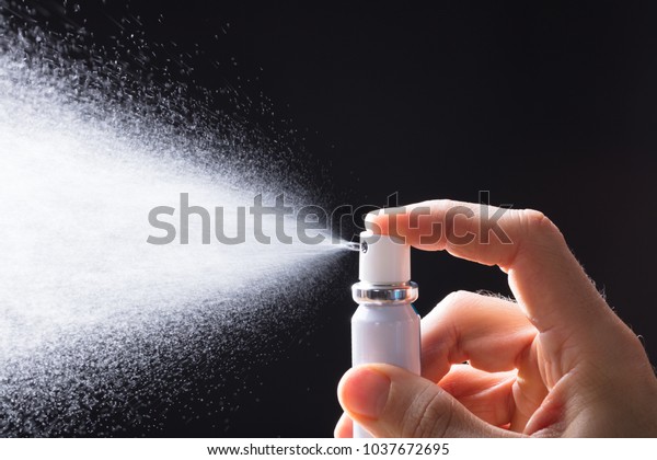 A Person\'s Hand Spraying Breath Freshener On\
Black Background