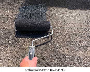 Person's Hand Using A Roller To Seal A Tarmac Driveway With Black Paint