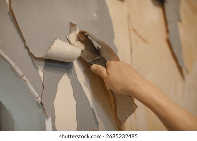 Person's hand using a scraper tool, removing old wallpaper during a home renovation or diy project, preparing for new paint