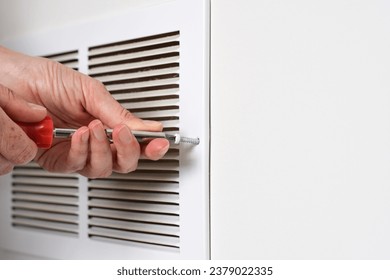 Person's hand using screwdriver to open return air vent for cleaning