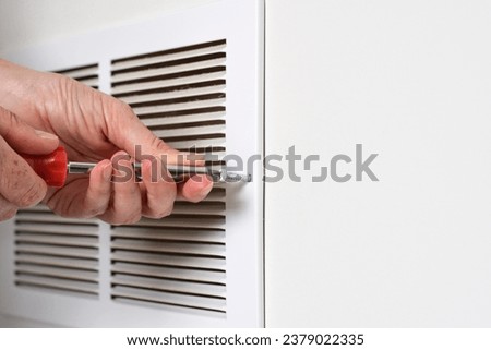 Person's hand using screwdriver to open return air vent for cleaning