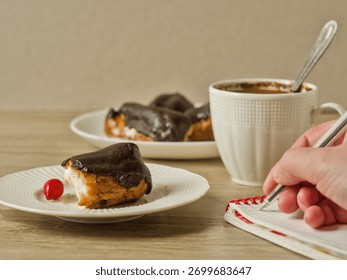 A person's hand writes in a small notebook during a coffee break with a pastry