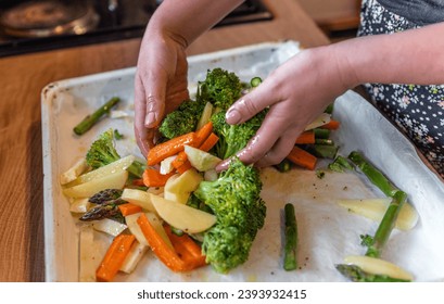 A person's hands arranging the raw sliced vegetables on an oven tray - Powered by Shutterstock