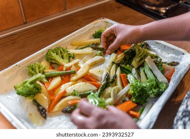 A person's hands arranging the raw sliced vegetables on an oven tray - Powered by Shutterstock