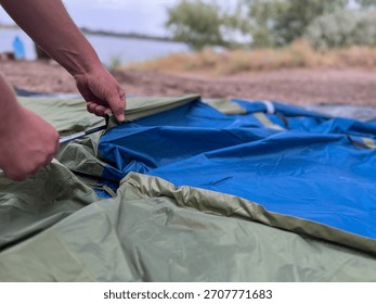 Person's hands assembling tent poles, preparing for outdoor camping near a lake