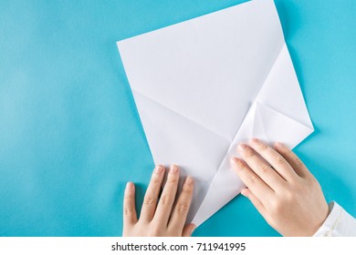 Person's Hands Folding A Paper Airplane On A Blue Background