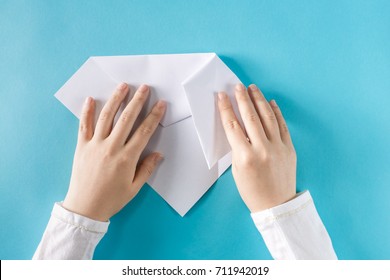 Person's Hands Folding A Paper Airplane On A Blue Background