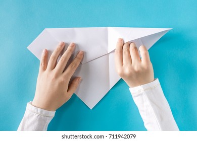 Person's Hands Folding A Paper Airplane On A Blue Background