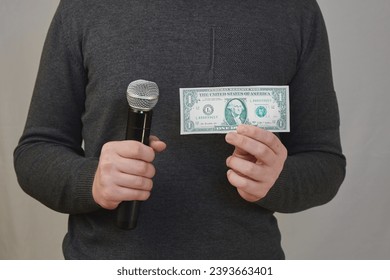 A person's hands holding a microphone in one hand and a one-dollar bill in the other. Tabloid press, buying votes from voters, paid-for commissioned reports