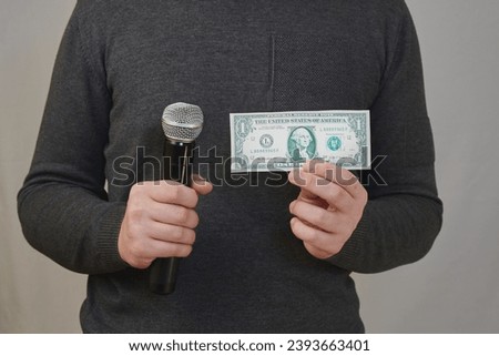 A person's hands holding a microphone in one hand and a one-dollar bill in the other. Tabloid press, buying votes from voters, paid-for commissioned reports