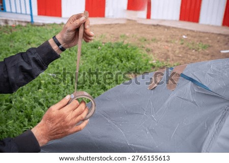 Person's hands patching a tent with tape, representing unsheltered living and poverty