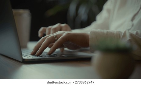 A person's hands with a ring are actively typing on a laptop keyboard, suggesting work or study in a comfortable setting