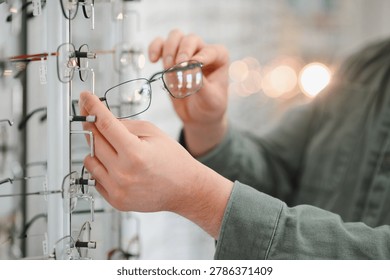 Person's hands selecting new pair of glasses from a large rack display in modern optical shop, focusing on a frame