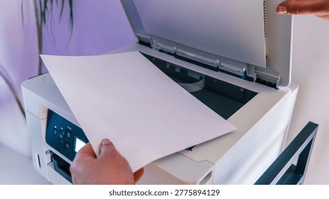 A person's hands are shown inserting a blank white sheet of paper into the input tray of a white multifunction printer, ready for scanning or copying