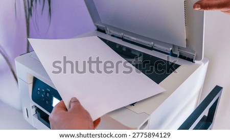 A person's hands are shown inserting a blank white sheet of paper into the input tray of a white multifunction printer, ready for scanning or copying