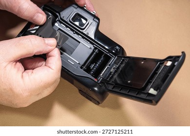 A person's hands are shown loading a roll of film into an old-fashioned 35mm camera, preparing to capture memories. Nostalgia for old tech