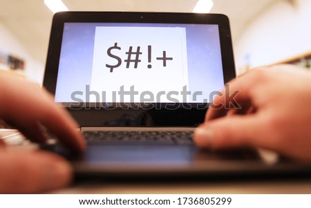 person's hands typing the work $#!+ on a keyboard of a laptop computer. White screen with large text. Swearing or cussing on a digital device. Creative concept for caught out at work. Logos removed