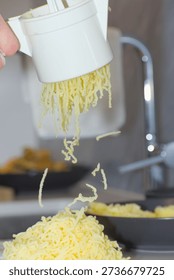 A person's hands use a white plastic manual potato ricer to press cooked yellow potatoes onto a pile of white flour on a kitchen countertop.