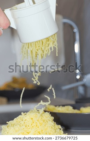 A person's hands use a white plastic manual potato ricer to press cooked yellow potatoes onto a pile of white flour on a kitchen countertop.