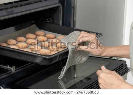 person's hands using an oven mitt to remove a tray of cookies from an oven
