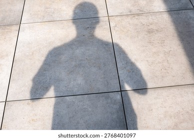 Person's shadow falling on a bright tiled ground, symbolizing presence and anonymity