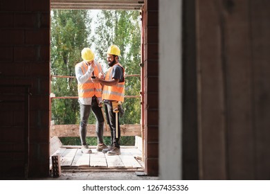 Persons Working In Construction Site. Latino Manual Workers Laughing And Using Smartphone For Internet And Social Media During Break