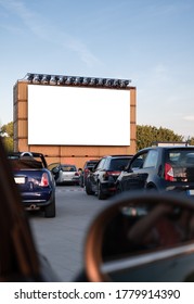 Perspective Of A Cinema Drive In Parking With Cars Parked In Front Of A Big White Screen To Watch Movies Or Films Inside The Car. Open Air Public Cinema Drive-in. Social Distance, Covid-19
