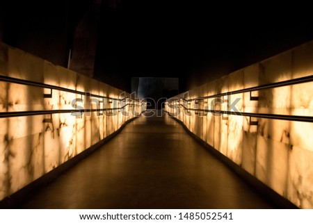 Perspective image of lit up walls, aluminium railings and cement walkway.