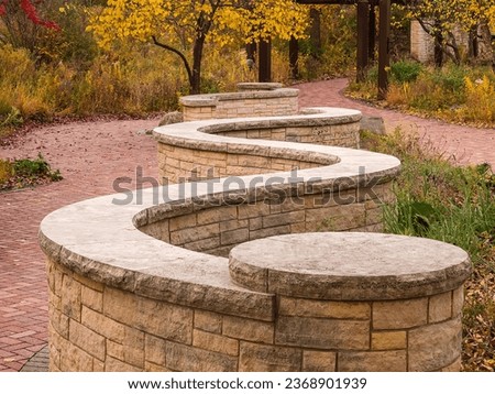 Perspective of a low, serpentine stone wall and ledge along a brick walkway in a county nature preserve on an October morning in northeast Illinois, USA, for motifs of landscaping