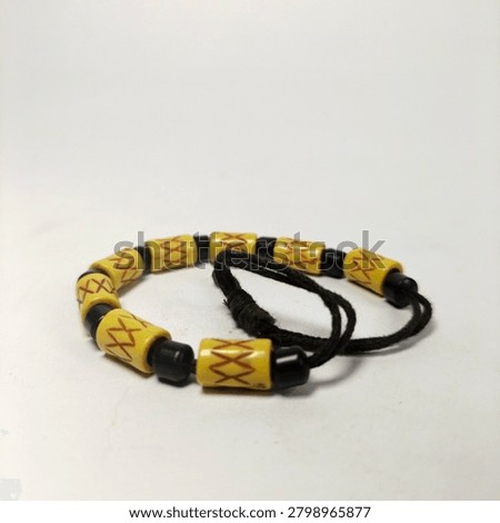 Perspective macro view of a circular tribal bead bracelet placed on a solid white surface. This shot captures the textured surface of the cream-yellow beads with hand-engraved cross patterns, combined with tiny glossy black spacers that create a bold color contrast suitable for ethnic fashion concepts.