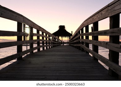 Perspective photo of vintage rustic wood jetty pier wharf deck bridge bridging over water in the Long Island Sound NY with fence line of lights and warm subdued pink mauve pastel warm sunset - Powered by Shutterstock