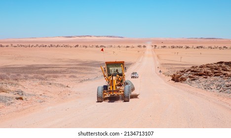 Perspective road background of Yellow grader smooths dirt road in namib deserts - Road grader smoothing a dirt road in a rural area - Namibia, Africa