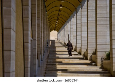 Perspective Shot Of Franciscan Monk Walking Away In Corridor Of Columns.